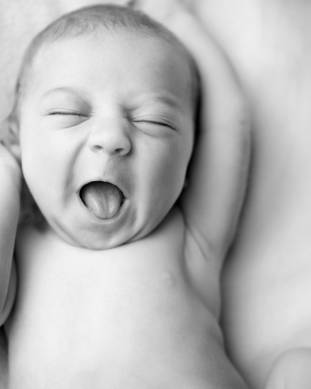 Black and white picture of a baby with closed eyes and open mouth, stretching its hands upwards