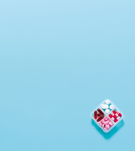 Tabletten in Rot, Rosa und Weiß in einer Box auf blauem Hintergrund angeordnet